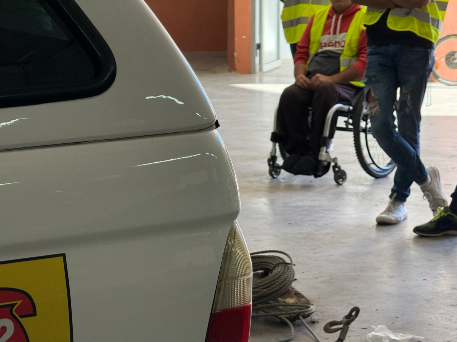 Personas con chalecos reflectantes, uno en silla de ruedas, cerca de un vehículo de emergencias.