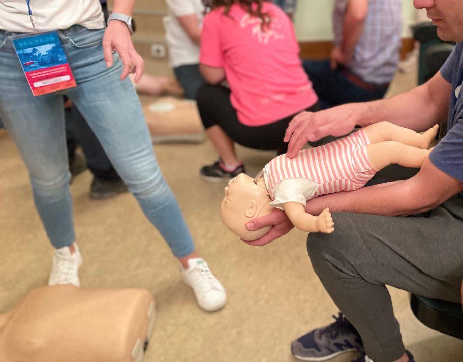 Una persona realiza RCP a un maniquí de bebé mientras otros participan en una actividad de entrenamiento.