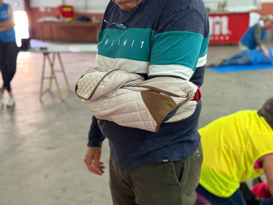 Inmovilización del brazo de una persona, con una chaqueta a modo de cabestrillo. Vista lateral.