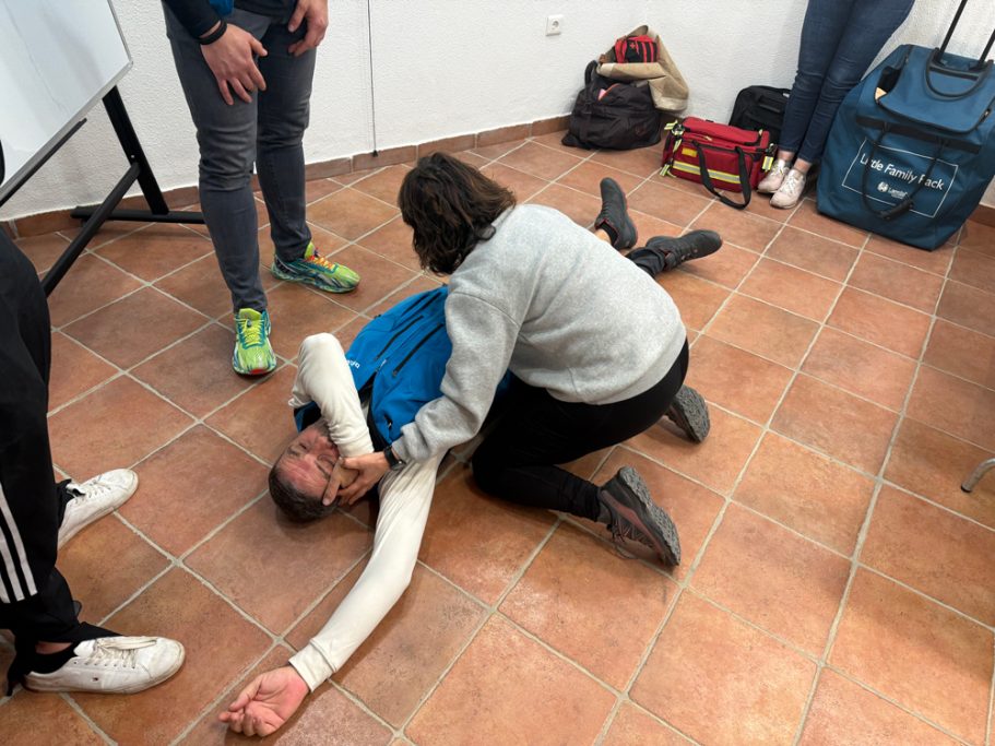 Una persona asiste a otra que está en el suelo, aparentemente lesionada, en un entorno formativo.