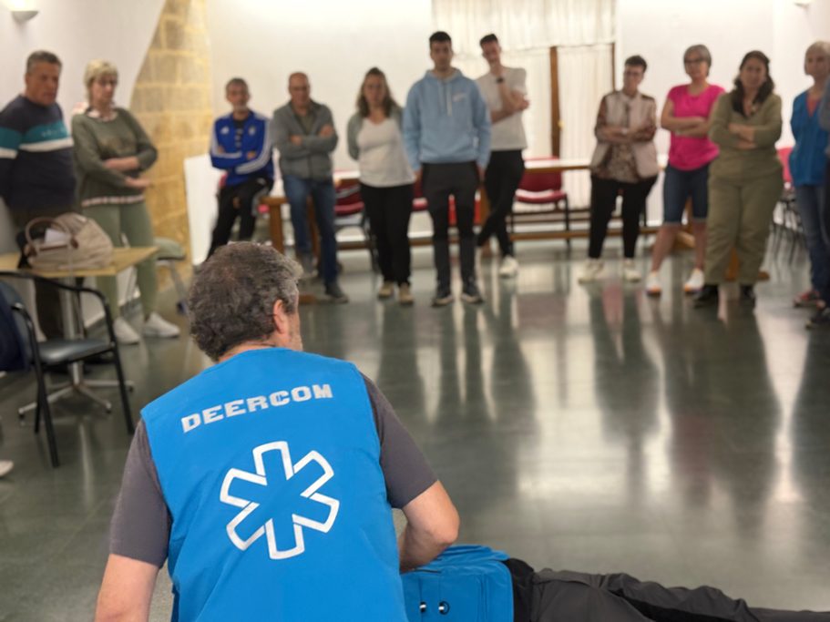 Instructor con chaleco azul de DEERCOM, enseñando a un grupo sobre primeros auxilios en una sala.