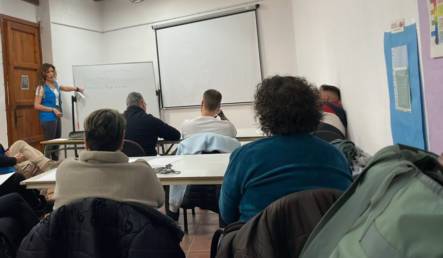 Una presentación en un aula con varias personas sentadas y una ponente de pie.
