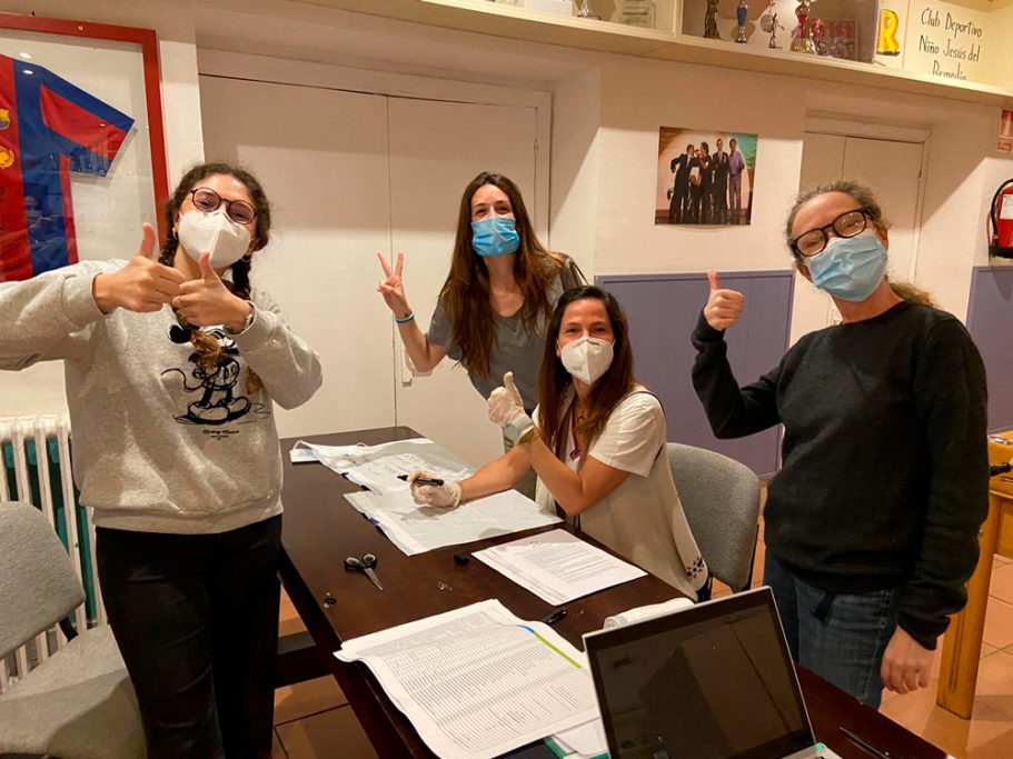 Equipo de logistica sonrientes con mascarillas en una mesa, haciendo gestos de aprobación.