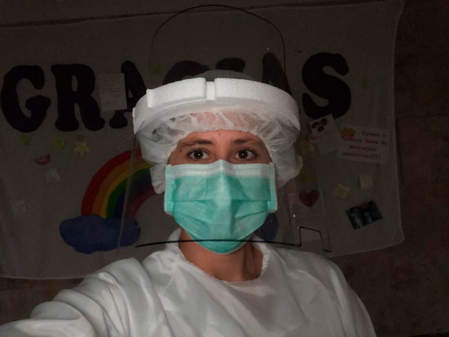 Profesional de la salud con gorro, mascarilla y pantalla, frente a un fondo con un agradecimiento.
