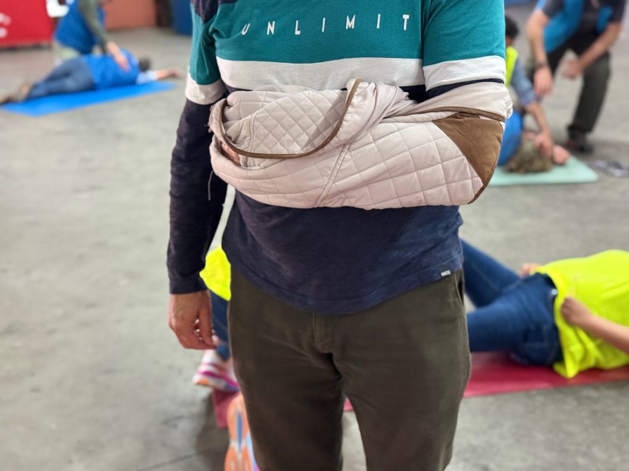 Inmovilización del brazo de una persona, con una chaqueta a modo de cabestrillo. Vista frontal.