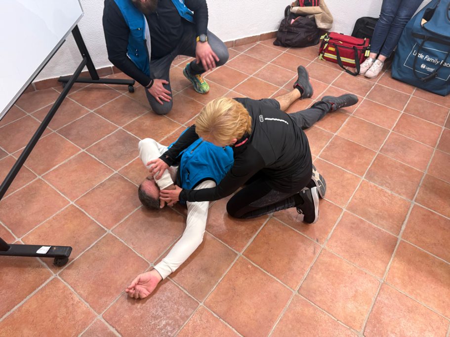 Persona en el suelo recibiendo primeros auxilios, con dos personas a su alrededor.