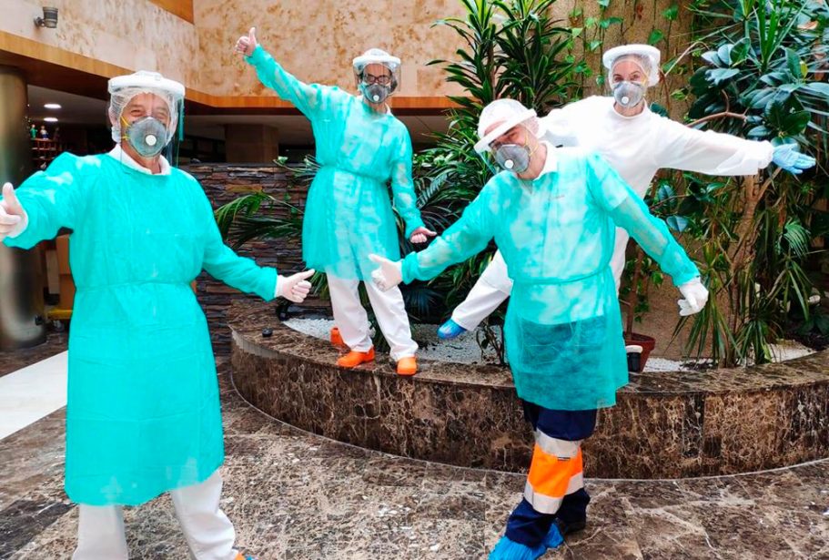 Cuatro profesionales de la salud en equipo de protección, con gestos de agradecimiento.
