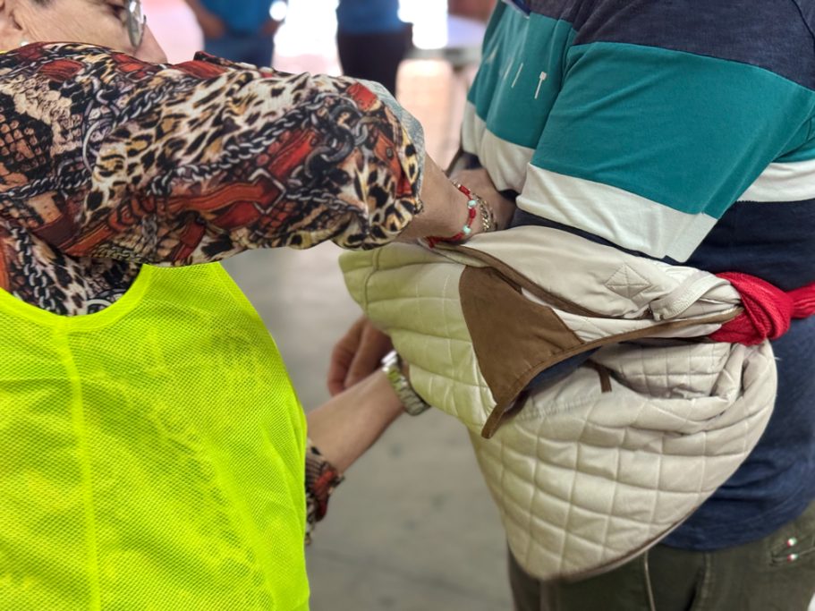 Mujer realizando inmovilización de brazo, con una chaqueta a modo de cabestrillo.