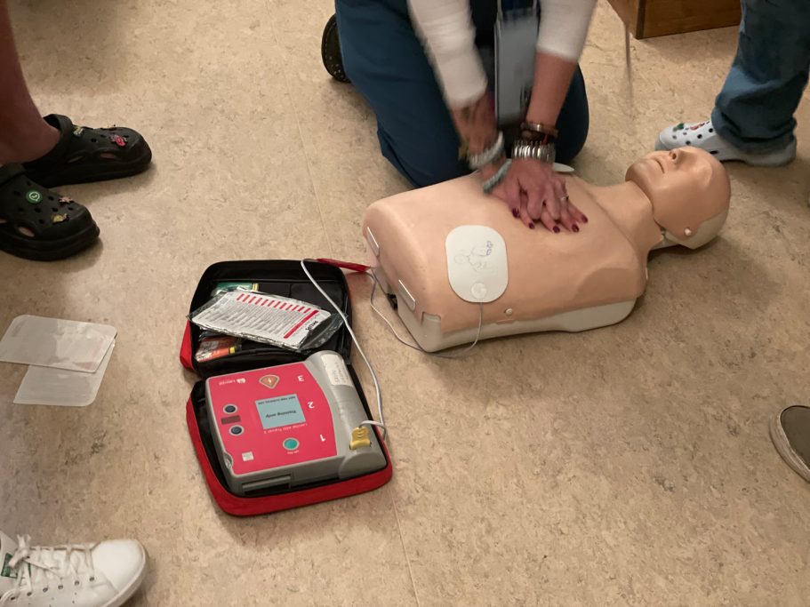 Una persona realiza RCP en un maniquí, cerca de un desfibrilador portátil.