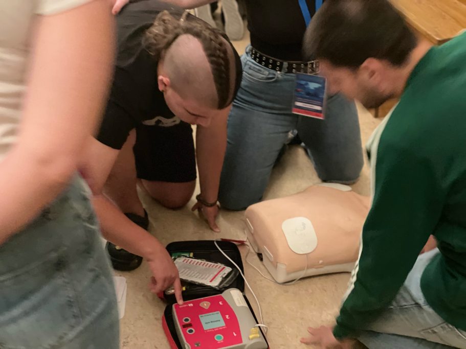 Jóvenes utilizando un desfibrilador de entrenamiento a un maniquí adulto.