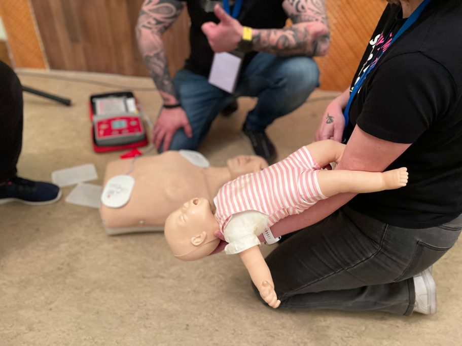 Persona arrodillada sosteniendo un maniquí de bebe RCP en una demostración de primeros auxilios.
